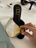 NOU Addison Mule: gold metallic leather upper with amber jewel embellishment and black stiletto heel.