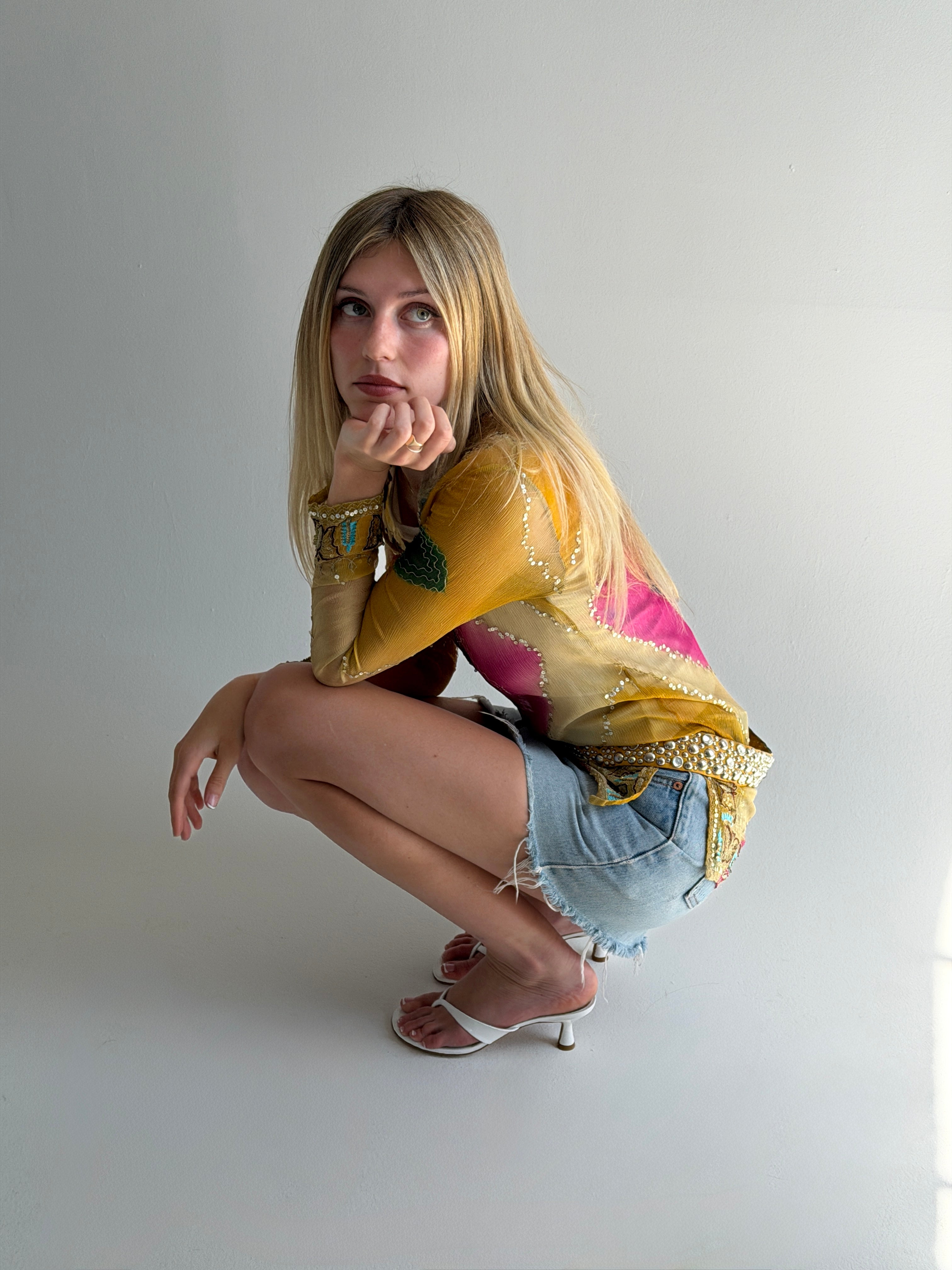 Woman in colorful top and denim shorts posing on a white background