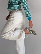 Person wearing a striped sweater and white pants, holding a blue high-heeled shoe.