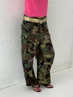 Person wearing camouflage pants and a pink top against a white wall.