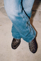 NOU The Driver loafers in burgundy leather with leopard print ponyhair, worn with blue jeans on a concrete floor.